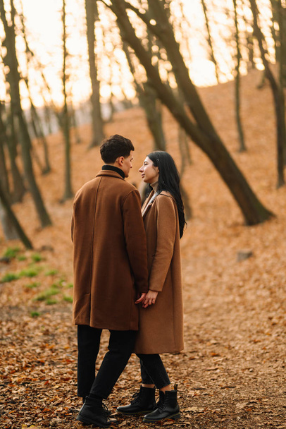 Stylish young couple outdoors on a beautiful autumn day in the forest. Young couple in love holding hands and walking through a park on a autumn day. The concept of youth, love and lifestyle. - Foto, Imagem
