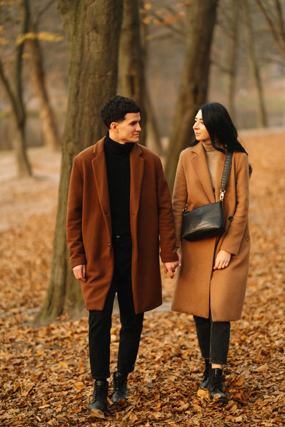 Stylish young couple outdoors on a beautiful autumn day in the forest. Young couple in love holding hands and walking through a park on a autumn day. The concept of youth, love and lifestyle. - Фото, зображення