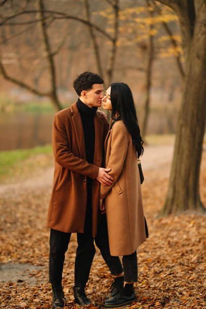 Stylish young couple outdoors on a beautiful autumn day in the forest. Young couple in love holding hands and walking through a park on a autumn day. The concept of youth, love and lifestyle. - Foto, immagini