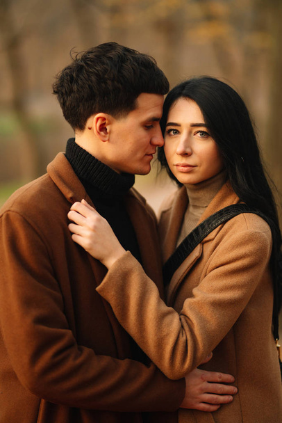 Stylish young couple outdoors on a beautiful autumn day in the forest. Young couple in love holding hands and walking through a park on a autumn day. The concept of youth, love and lifestyle. - Foto, Imagen