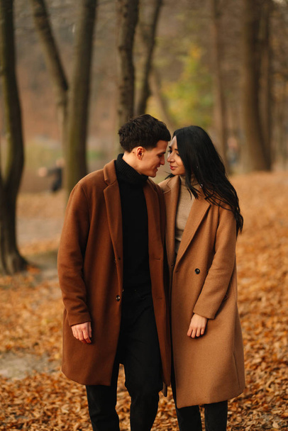 Stylish young couple outdoors on a beautiful autumn day in the forest. Young couple in love holding hands and walking through a park on a autumn day. The concept of youth, love and lifestyle. - Фото, изображение