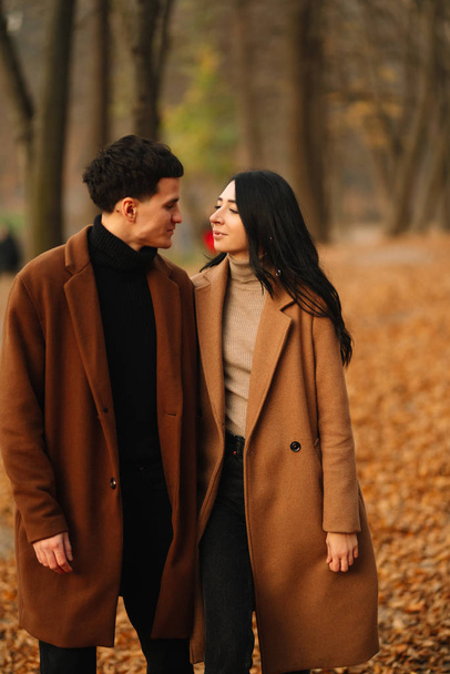 Stylish young couple outdoors on a beautiful autumn day in the forest. Young couple in love holding hands and walking through a park on a autumn day. The concept of youth, love and lifestyle. - Fotografie, Obrázek