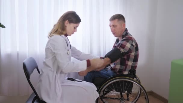 Sağlık hizmeti, tekerlekli sandalyedeki bir hasta doktoru muayene eder ve tıbbi bir aletle ona uygulanan baskıyı ölçer. - Video, Çekim