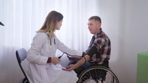 Sozialarbeiterin misst bei körperlicher Untersuchung Druck mit professionellem Hilfsmittel auf Patienten im Rollstuhl - Filmmaterial, Video