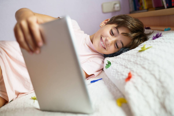Мила дівчина використовує планшетний комп'ютер у своїй спальні
 - Фото, зображення