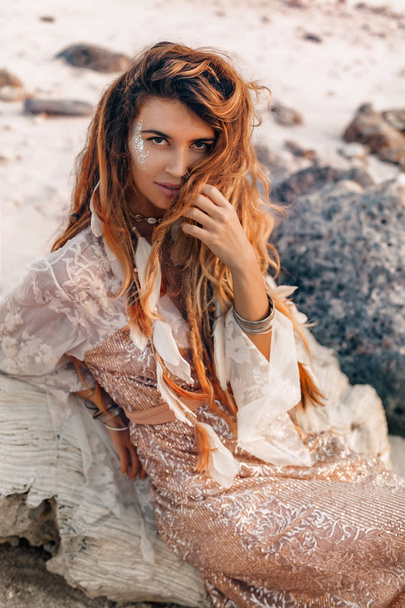 young fashionable woman sitting on the stone beach portrait - 写真・画像