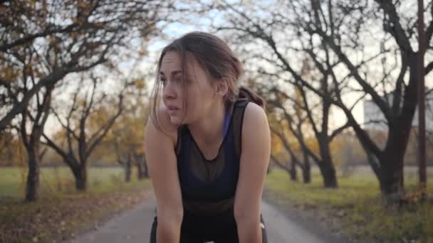 Portrait of tired sportive girl resting on alley in the autumn park as two strong sportsmen running by. Young Caucasian woman starting chasing handsome guys. Healthy lifestyle concept - Metraje, vídeo