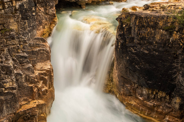 Длинная гладкая молочная вода водопада, пробивающегося сквозь узкое отверстие скалы
 - Фото, изображение