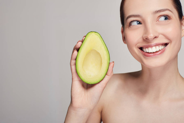 Profile side portrait of brown-haired attractive nude lady with perfect pure skin with avocado in the hand and smiling with teeth and looking at side - 写真・画像