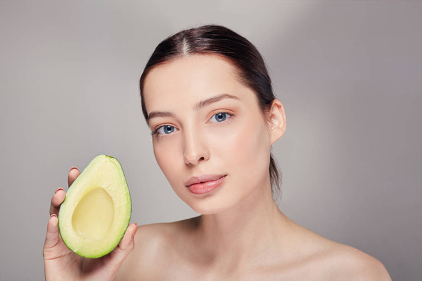 pensive tender calm brown-haired nude lady looking streight with perfect pure shine skin with avocado in the right hand - Fotó, kép