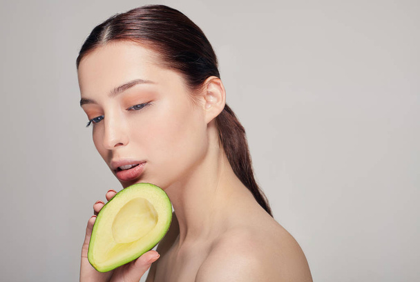 portrait of attractive tender calm brown-haired nude lady with avocado in the hand with perfect skin looking down - Photo, Image