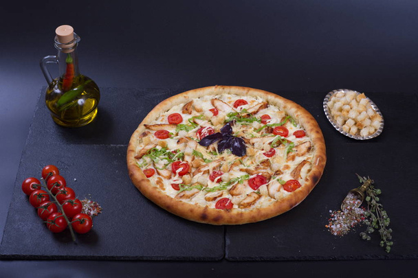 pizza with chicken breast, croutons and vegetables lies next to spices on a dark background - Photo, image