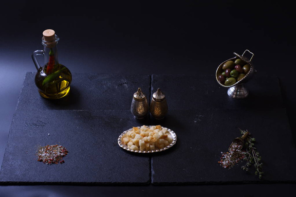 croutons lie next to a jug of olive oil and spices on a dark background - Foto, Imagen