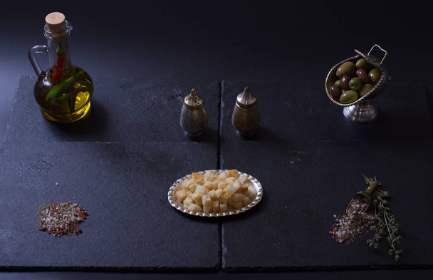 croutons lie next to a jug of olive oil and spices on a dark background - Fotoğraf, Görsel