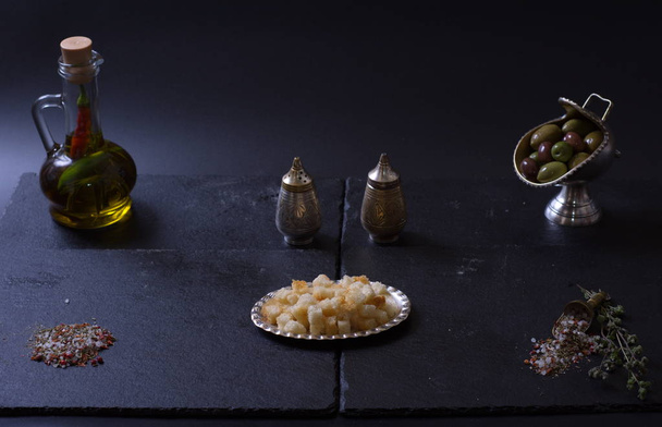croutons lie next to a jug of olive oil and spices on a dark background - Fotó, kép