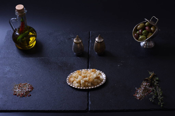 croutons lie next to a jug of olive oil and spices on a dark background - Photo, Image