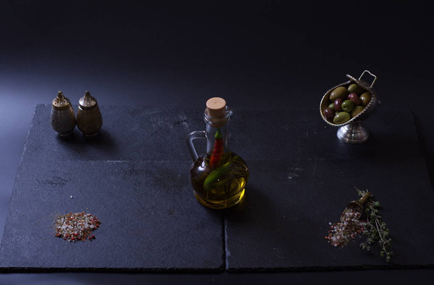 a jug of butter stands next to vegetables and spices on a dark background - Foto, Imagen