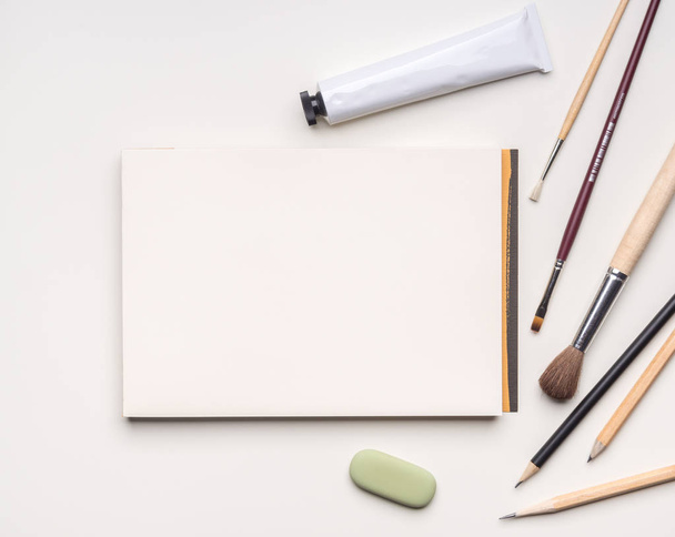 Blank flat template of sketchbook with various art tools on white background - Фото, изображение
