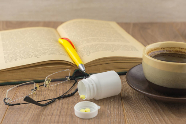 Sonolência: pílulas de cafeína perto da caixa da pílula, livro velho, óculos
 - Foto, Imagem