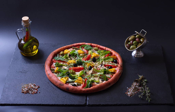 vegetarian pizza with tomatoes, peppers and vegetables lies next to spices on a dark background - Photo, image