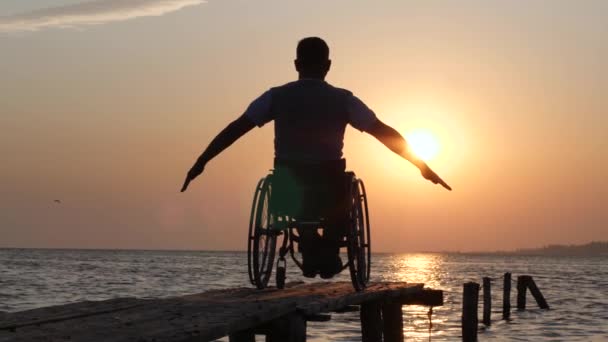sairas mies pyörätuolissa rentoutuu ja nostaa kätensä taustalla oranssi taivas kesämatkalla
 - Materiaali, video