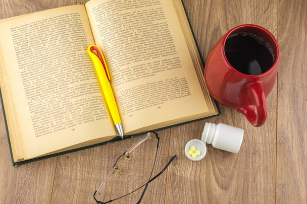 Sonolência: pílulas de cafeína perto da caixa da pílula, livro velho, óculos
 - Foto, Imagem