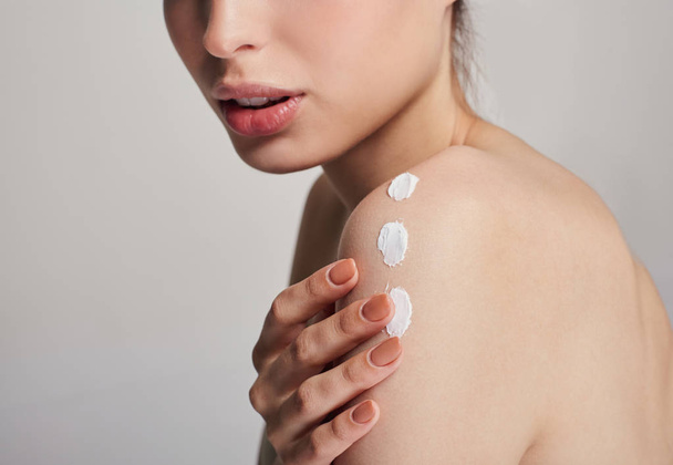 Close-up shot of a young girl with clean skin applying cream with three strokes on her shoulder. Body cream on the shoulder. Beauty and spa care. - Foto, Bild