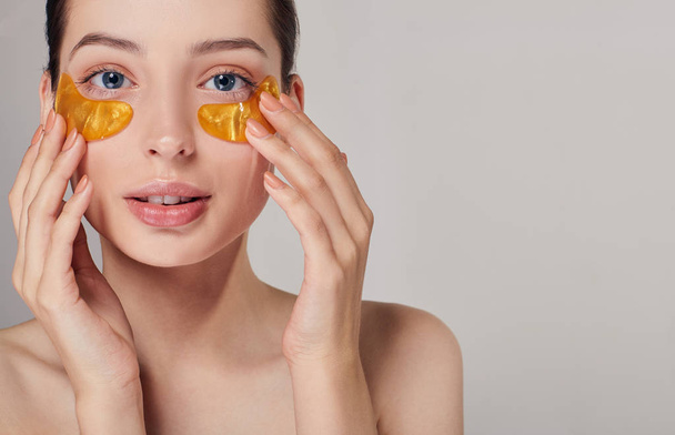 girl applying golden collagen patches under the eyes. Remove wrinkles and dark circles. A woman takes care of delicate skin around her eyes. Cosmetic procedures. Facial skin care. - Foto, imagen