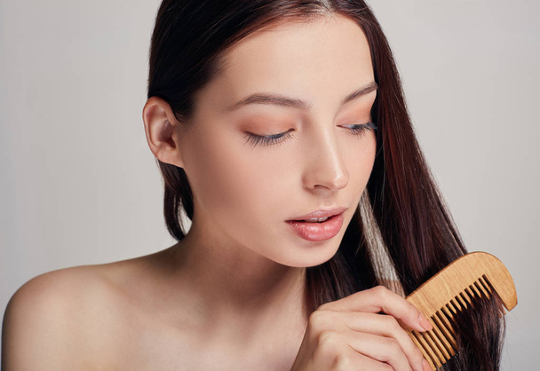 Close up a tender girl with a playful mood combs her hair with a light brown comb on the background looks - Photo, Image