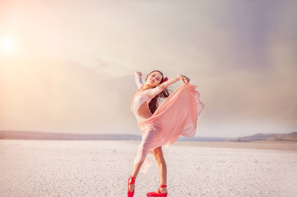 girl ballerina dancer in a pink dress on a snow-white salty dried lake. Fantastic landscape and a girl in red punata and a pink dress. - Valokuva, kuva