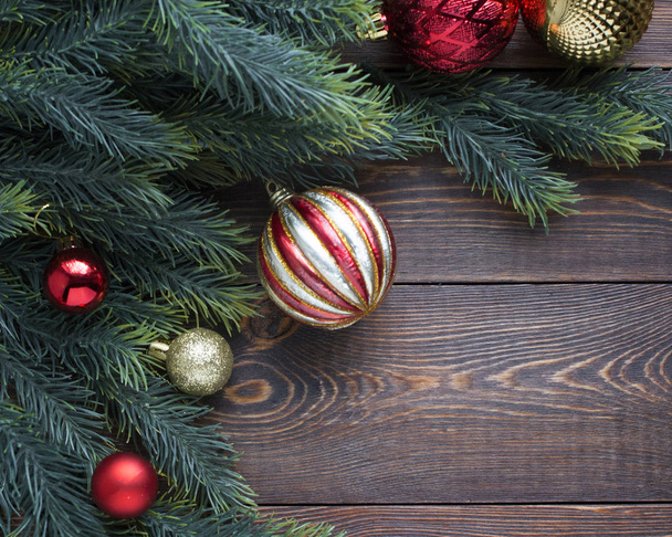 Rámeček z jedlových větví, červené a zlaté vánoční stromeček koule na dřevěném hnědém pozadí.  - Fotografie, Obrázek