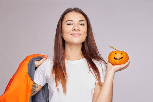 Zadowolony spokojny mieszane wyścigi młoda kobieta zbieranie dyni, pochyla głowę, uśmiecha się szeroko, trzyma pomarańczową kurtkę, cieszy się jesienią czasu i świąt, odizolowany. Tradycyjny symbol Halloween w rękach damy. - Zdjęcie, obraz