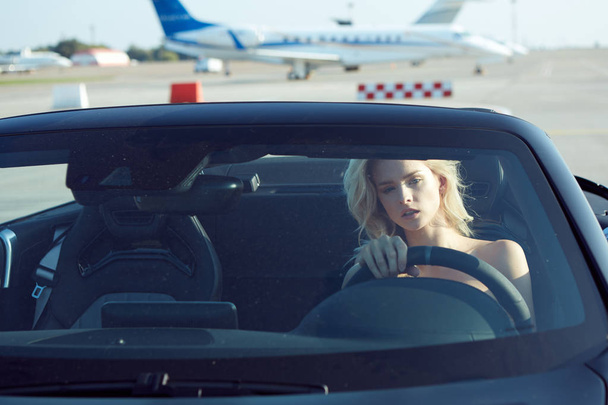 One glamorous blonde woman sit in cabriolet car, glamour girl inside cabrio auto on the runway. No retouch. - Фото, изображение
