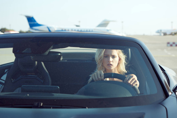 One glamorous blonde woman sit in cabriolet car, glamour girl inside cabrio auto on the runway. No retouch. - Foto, Imagem