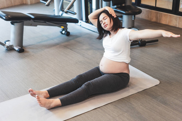 Active pregnant woman exercising  in fitness center at yoga room.  - Photo, Image