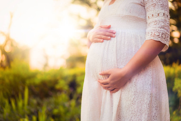 Έγκυος γυναίκα αισθάνεται ευτυχισμένη με τη νέα ζωή στο σπίτι κήπο, ενώ φροντίζει το παιδί της. Οι νέοι περιμένουν μητέρα κρατώντας το μωρό σε έγκυο κοιλιά. Προγεννητική φροντίδα μητρότητας και εγκυμοσύνη γυναίκα έννοια. - Φωτογραφία, εικόνα