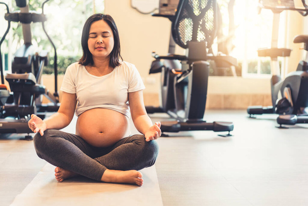 Active pregnant woman exercising  in fitness center at yoga room.  - Photo, Image