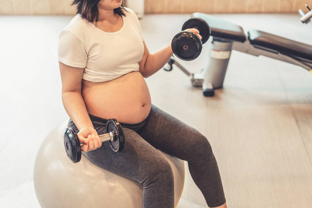 Active pregnant woman exercising  in fitness center at yoga room.  - Фото, зображення