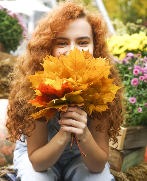 Autumn time. Ginger curly attractive girl with opened eyes wearing trendy autum color yellow shirt  holding yellow bouquet of maple leaves near face. Enjoy autumn season. smiley happy face. - Fotografie, Obrázek