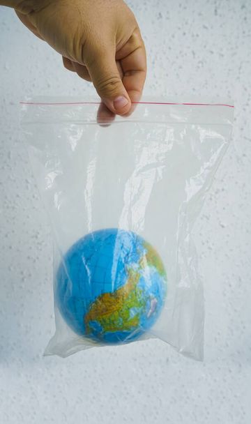 Close up male  hand hold in plastic bag Earth world globe isolated on white background. - Valokuva, kuva