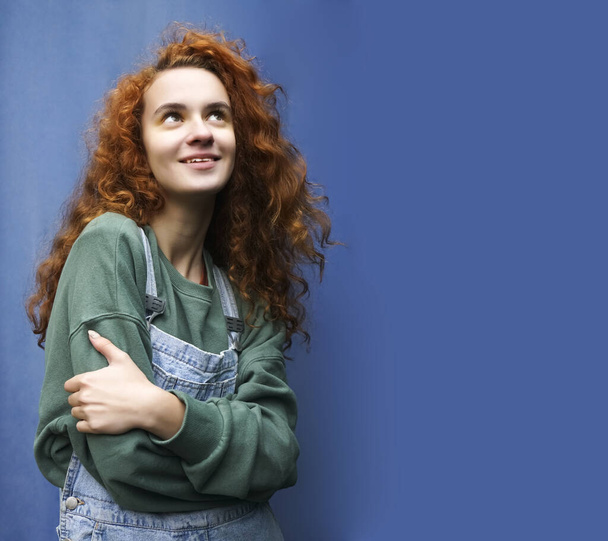 Portrait of young red-haired smiling woman against blue metal fence background. - Foto, afbeelding