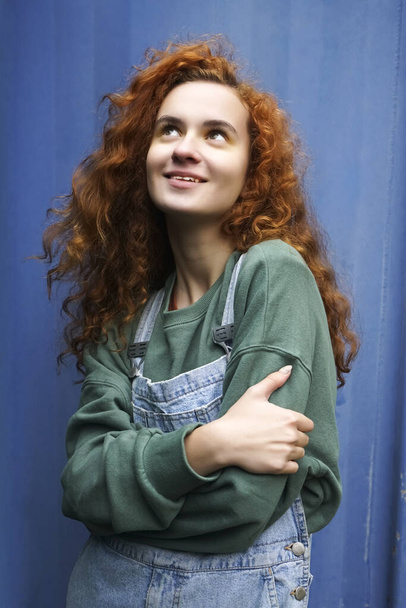 Portrait of young red-haired smiling woman against blue metal fence background. - Fotó, kép