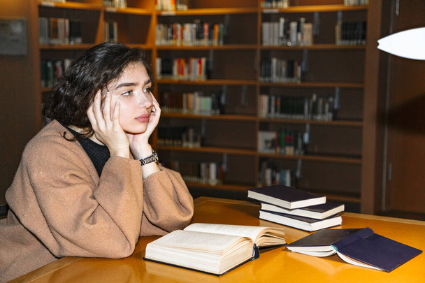 Tyttö kirjastossa istuu kirjojen ääressä ja ajattelee:
 - Valokuva, kuva