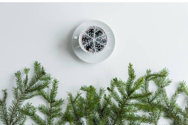 cup of black coffee and glowing snowflake in spruce branches on a white table. Christmas and New Year concept. Coffee art. Flat lay, top view.  - Fotó, kép