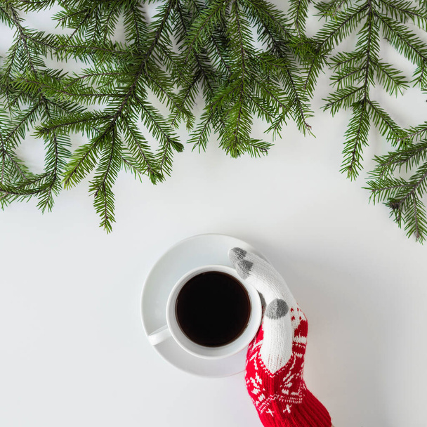 Female hands in the winter gloves with cup of black coffee in spruce branches on a white table. Christmas and New Year concept. Coffee art. Flat lay, top view. Instagram - Фото, зображення
