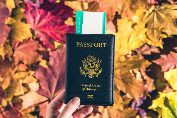 American passport with boarding pass in the woman hand maple leaves background in the autumn forest.  Travel Concept. Top view. Indian summer. - Zdjęcie, obraz