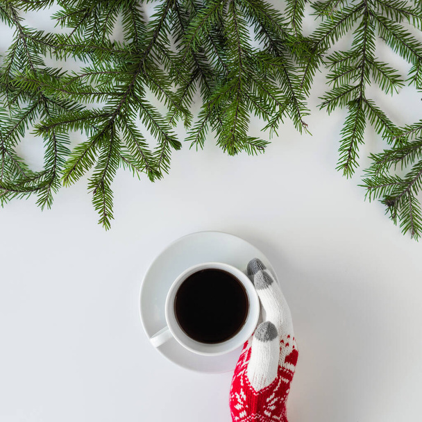Female hands in the winter gloves with cup of black coffee in spruce branches on a white table. Christmas and New Year concept. Coffee art. Flat lay, top view. Instagram - Фото, зображення