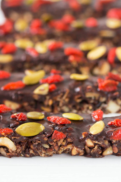 Vegan chocolate bars with granola, nuts, pumpkin and chia seed, goji berries. Homemade snack. Super energy bars on a white wooden background. - Foto, Bild
