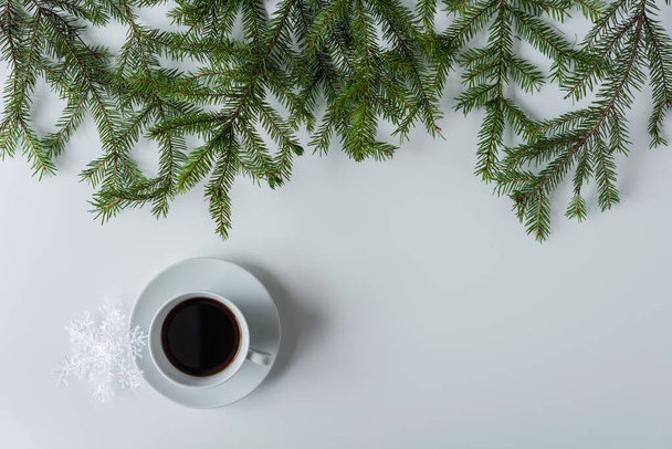 Female hands in the winter gloves with cup of black coffee and glowing snowflake in spruce branches on a white table. Christmas and New Year concept. Coffee art. Flat lay, top view.  - Photo, image