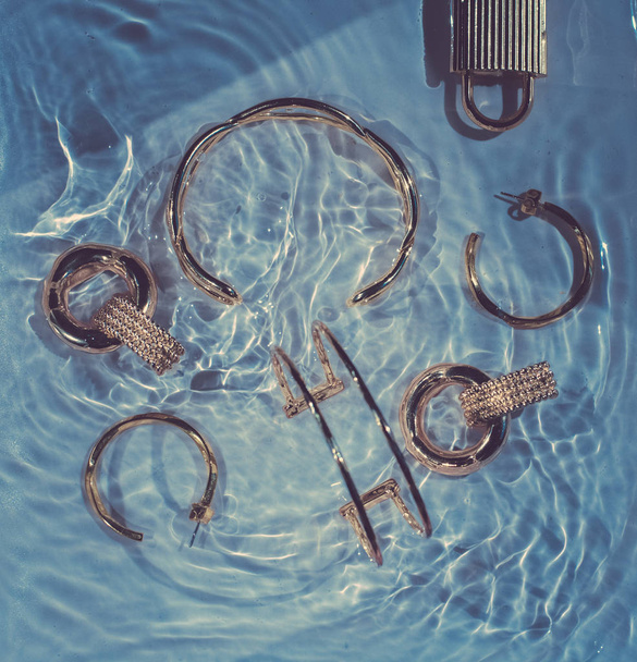 Golden bracelets, earrings, rings, jewelery on blue water backgr - Photo, Image